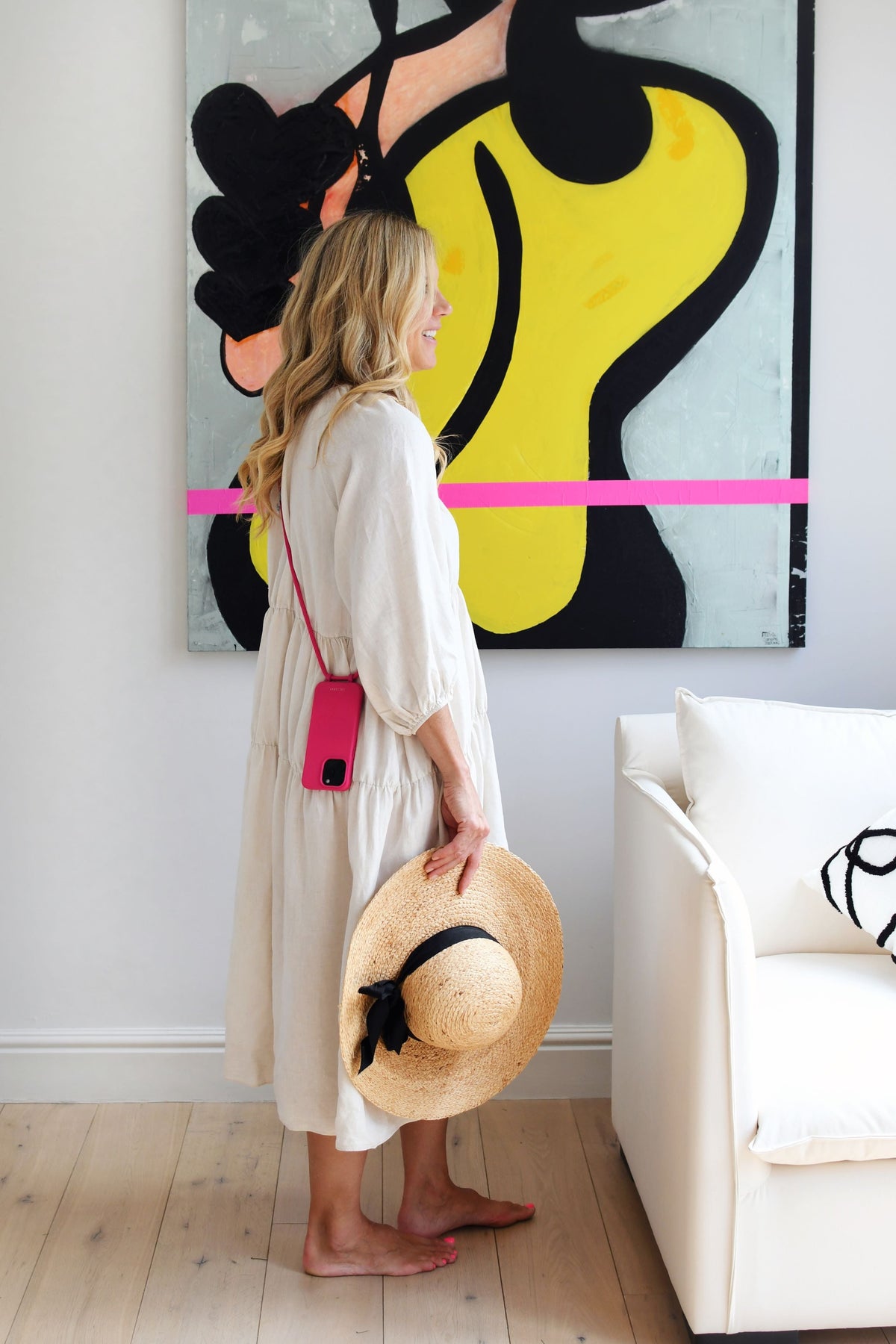 a woman standing in front of a painting holding a hat